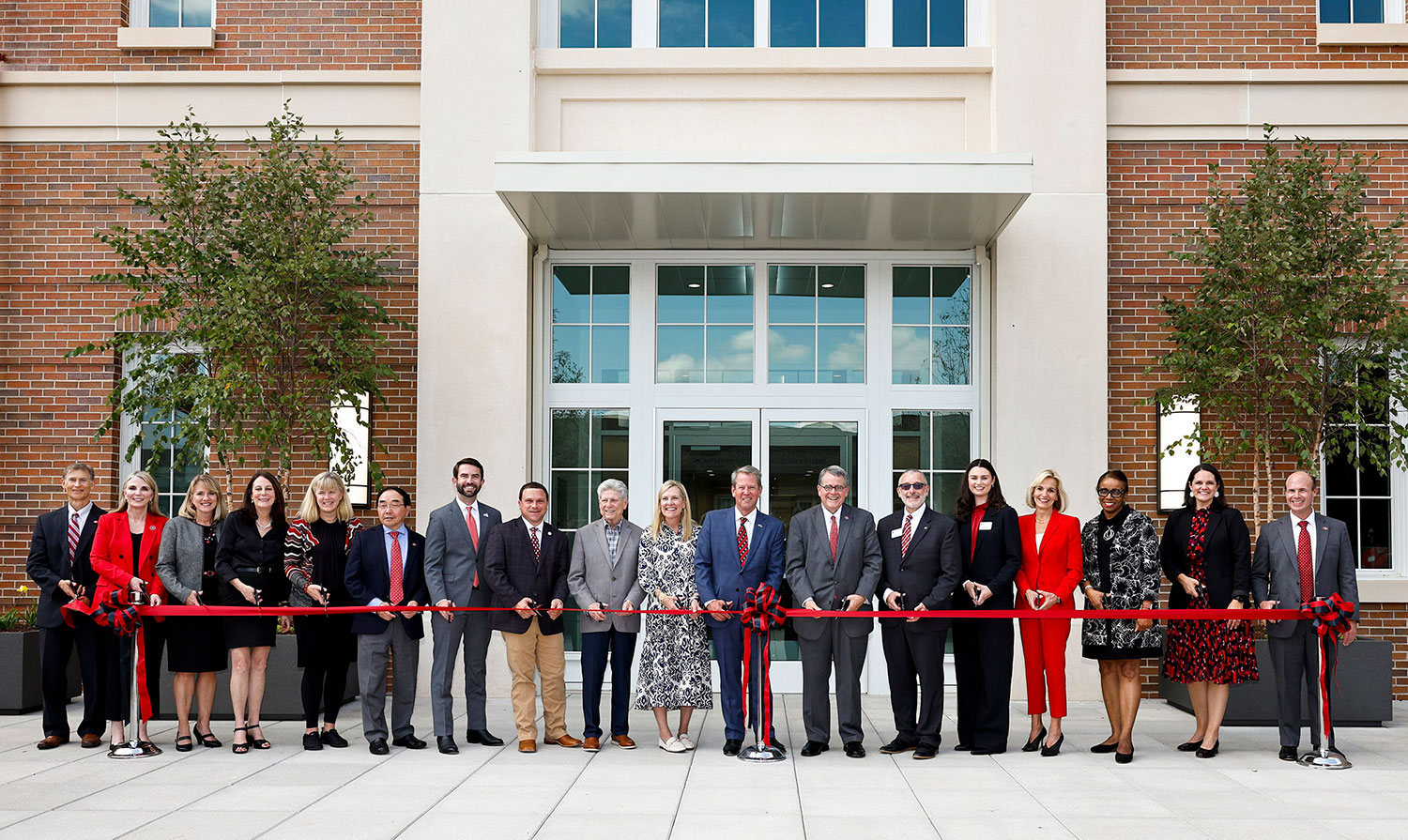 People lined up in front of a building, holding a red ribbon